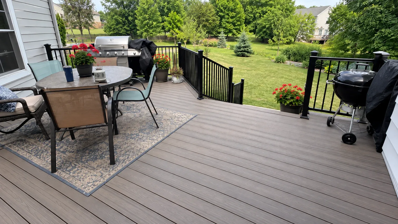 A composite deck with dark metal railings at sunset, steps rising to an upper tier beside the house